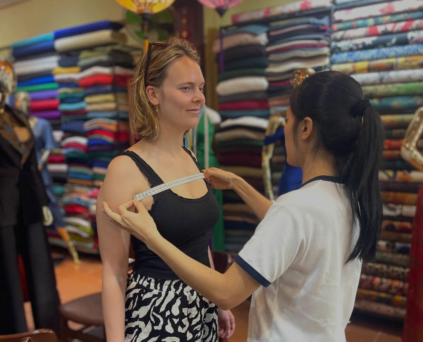 The tailor takes customers’ measurements for custom-made outfits.